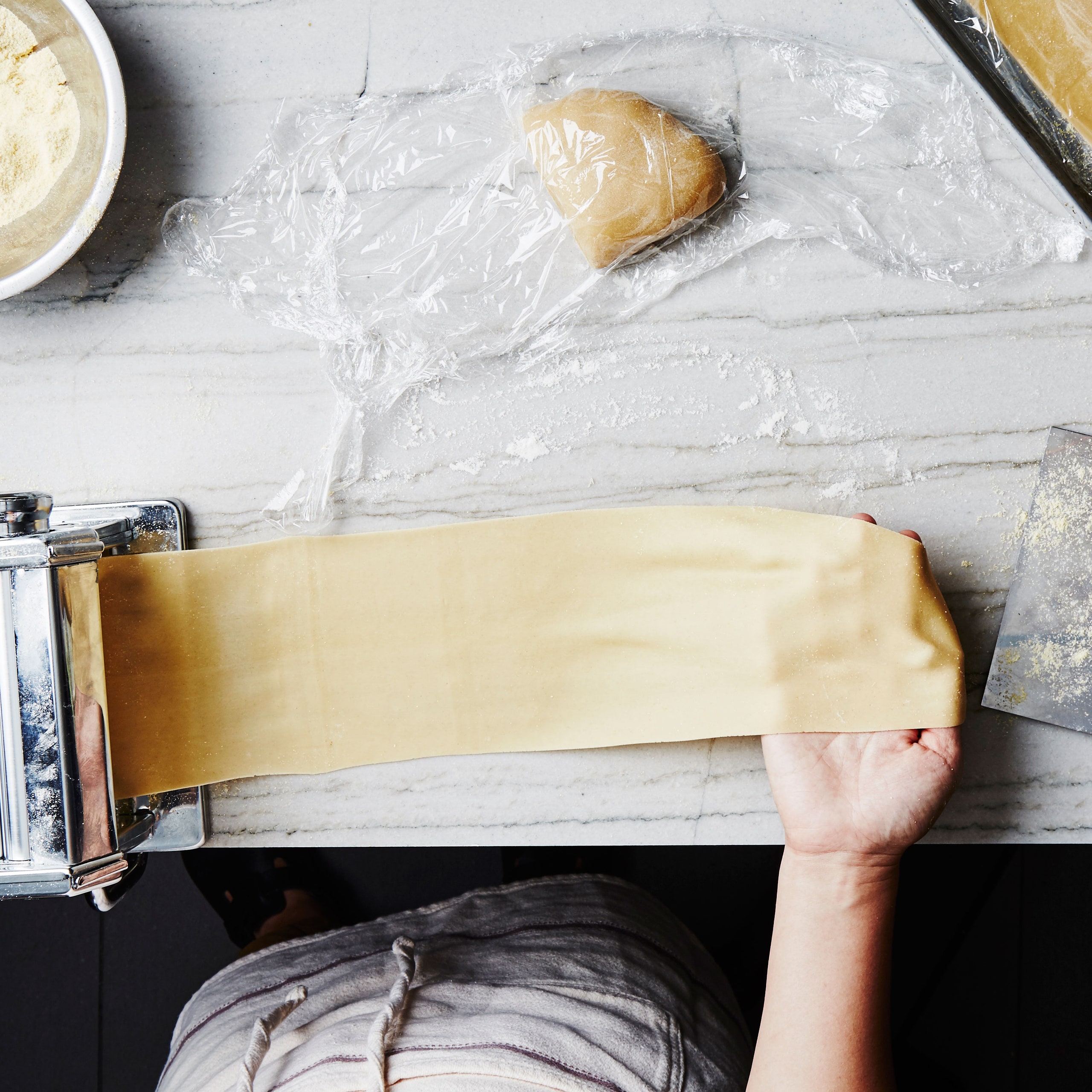 A person processing pasta dough through a countertop pasta machine.